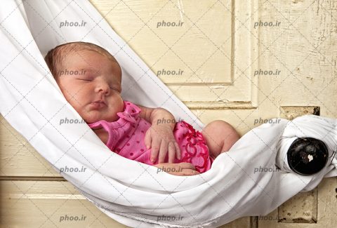 عکس نوزاد خوابیده با لباس صورتی در یک گهواره سفید