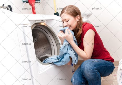 عکس با کیفیت زن نشسته در کنار لباسشویی و در حال بو کردن حوله ی خوشبو