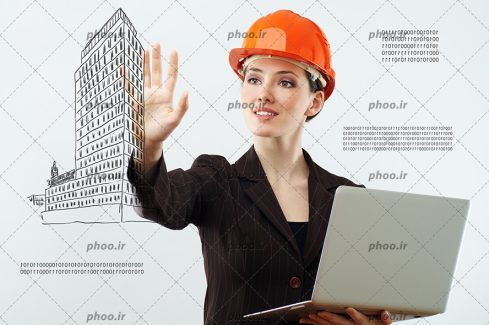 عکس با کیفیت مهندس ساختمان با کلاه ایمنی نارنجی و لپ تاپ به دست در حال تاچ کردن صفحه مانیتور شیشه ای و اسکیس ساختمان