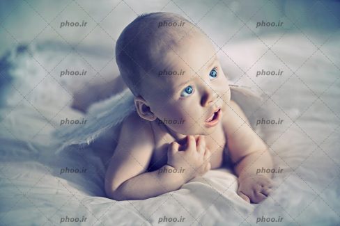 عکس با کیفیت نوزاد با چشم های آبی دراز کشیده بر روی پارچه سفید