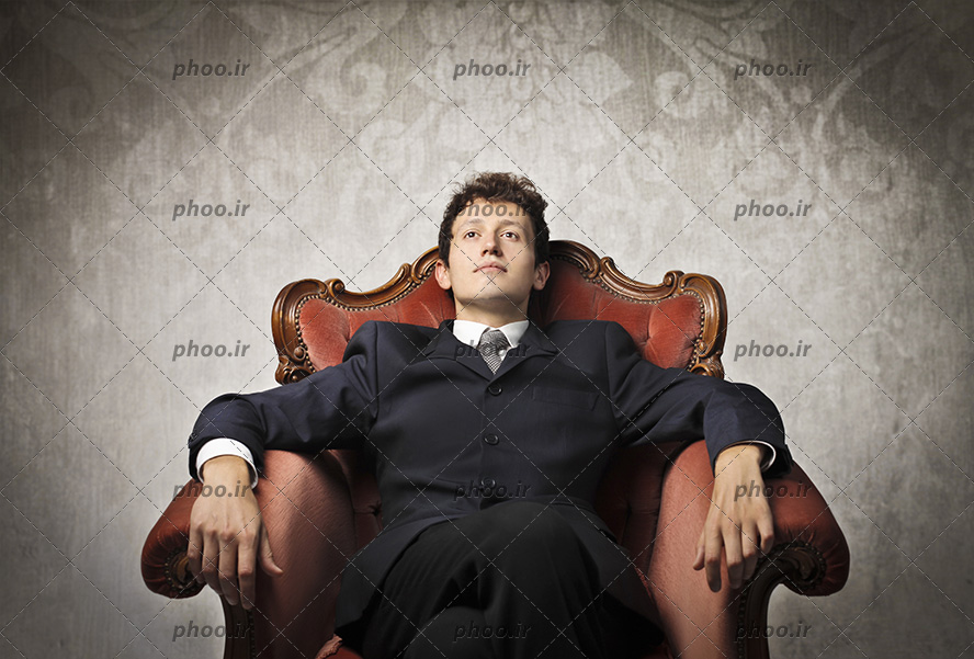 عکس با کیفیت مرد با کت و شلوار مشکی نشسته بر روی مبل