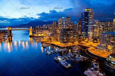 عکس با کیفیت آسمان در حال تاریک شدن و شهر زیبا و نورانی در کنار دریاچه