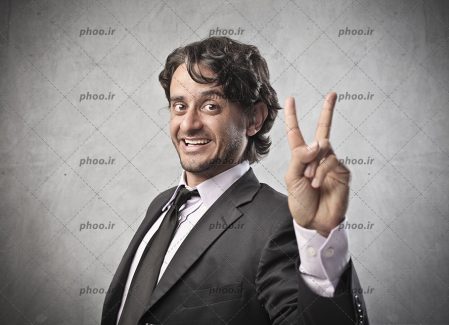 عکس با کیفیت مرد با کت و شلوار طوسی و در حال نشان دادن عدد پیروزی با دست