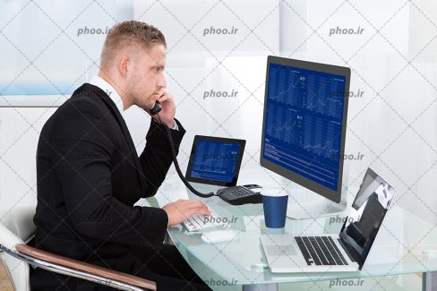 عکس با کیفیت مرد در حال صحبت با تلفن و در حال نگاه کردن به مانیتور