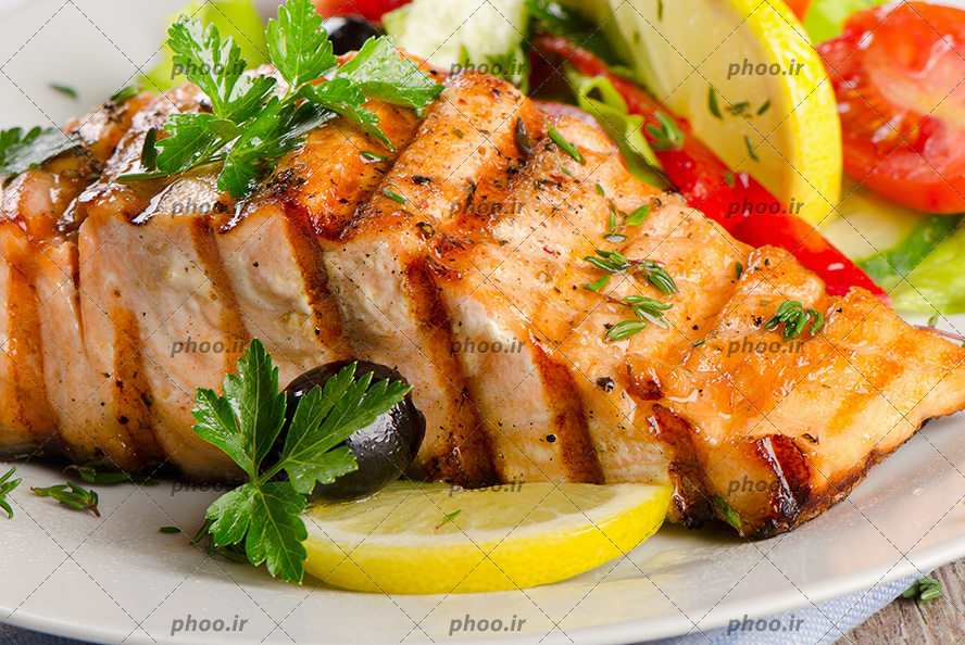 عکس با کیفیت ماهی پخته شده در ظرف با تزئین گوجه و زیتون و لیمو ترش