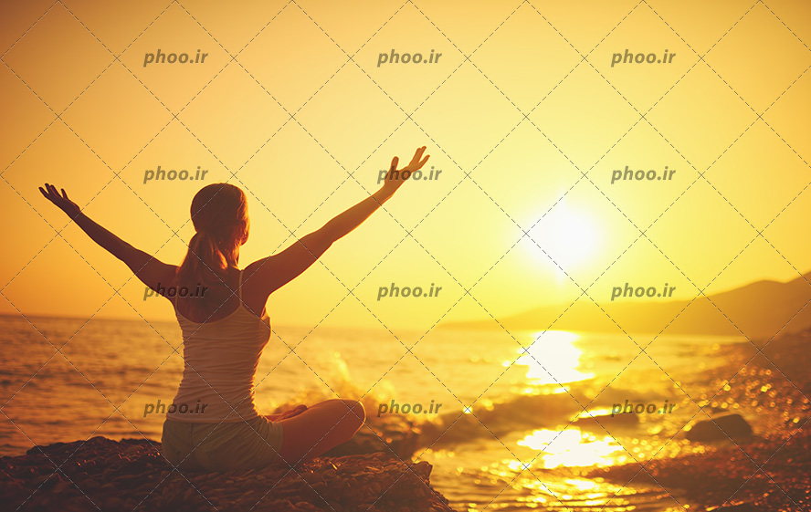 عکس با کیفیت زن در حال مدیتیشن در کنار دریا و آسمان در حال طلوع