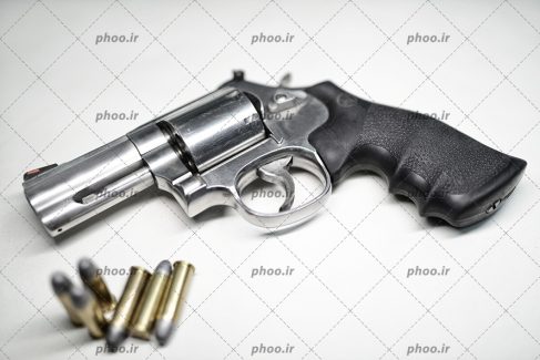 عکس با کیفیت فشنگ ها در کنار هفت تیر در پس زمینه سفید