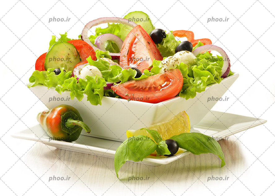 عکس با کیفیت سالاد سبزیجات در پیاله سفید چینی قرار گرفته بر روی بشقاب سفید چینی و تزئین شده با برگ نعناع و لیمو و فلفل قرمز