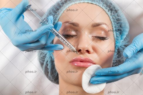 عکس با کیفیت پزشک با دستکش های آبی در حال تزریق ژل به لب های زن با چشم های بساه و کلاه آبی بر سر