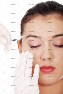 عکس با کیفیت پزشک با دستکش های سفید در حال تزریق ژل با سرنگ به صورت زن زیبا