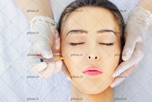 عکس با کیفیت سرنگ در دست پزشک و پزشک در حال تزریق ژل به گونه زن