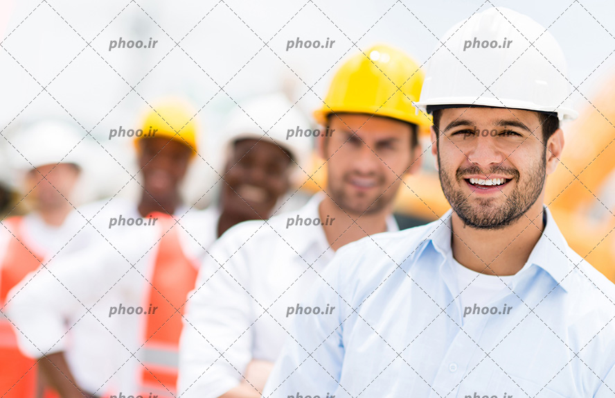 عکس با کیفیت مهندسین ساختمان در کنار یکدیگر به صورت ردیفی و کلاه ایمنی بر سر و در حال لبخند زدن