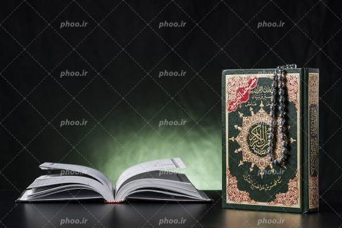 عکس با کیفیت دو قرآن کریم در کنار یکدیگر و تسبیح بر روی قرآن و پس زمینه به رنگ مشکی و سبز
