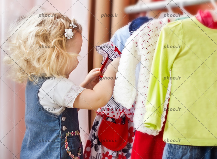 عکس با کیفیت کودک کوچک زیبا در حال گشتن لباس ها در رگال