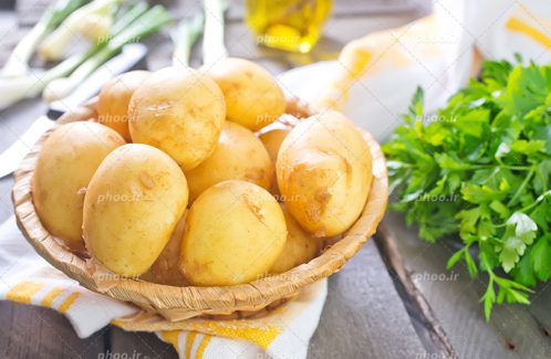 عکس با کیفیت سیب زمینی داخل ظرف حصیری در کنار سبزیجات و پارچه سفید