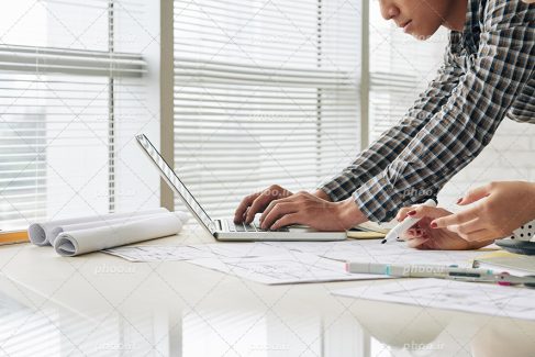 عکس با کیفیت مرد مهندس ایستاده در حال کارکردن با لپ تاپ و زن در حال توضیح دادن پلن و نقشه