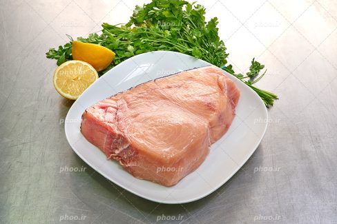 عکس با کیفیت ماهی خام داخل ظرف سفید در کنار مخلفات سبزی و لیمو ترش