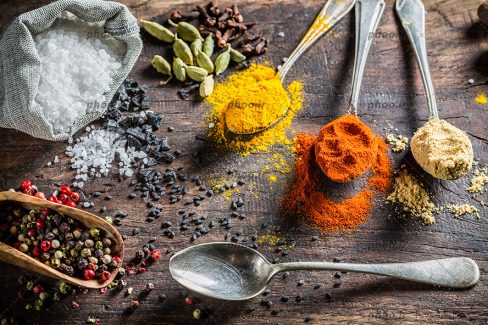 عکس ادویه هایی در قاشق های کوچک و دانه های ریخته روی تخته چوبی