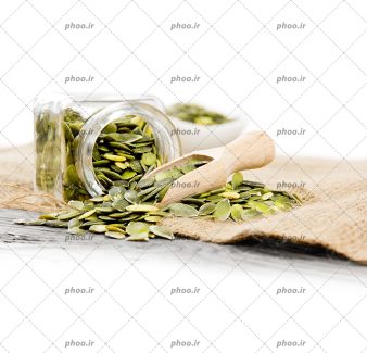 عکس تخمه کدو در ظرف شیشه ای و روی زمین در پس زمینه سفید