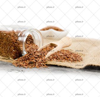 عکس دانه های کتان ریخته روی زمین و در ظرف شیشه ای در پس زمینه سفید