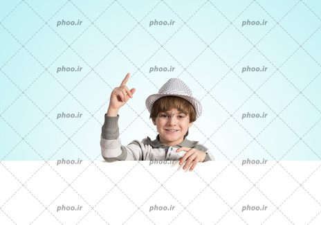 عکس پسر بچه با لبخند ایستاده پشت بنر سفید در پس زمینه آبی