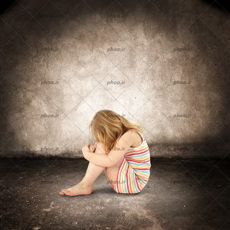عکس با کیفیت دختر کوچک غمگین و افسرده نشسته در پس زمینه قهوه ای
