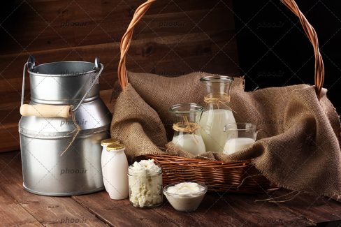 عکس لبنیات در ظرف های شیشه ای روی زمین و داخل سبددر پس زمینه چوبی