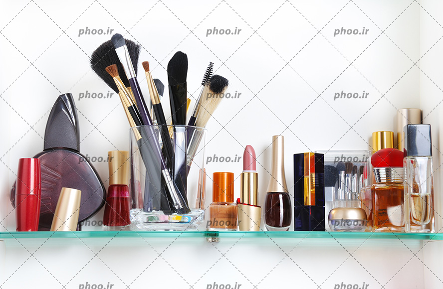 عکس لوازم آرایشی مختلف روی طاق شیشه ای در زمینه سفید