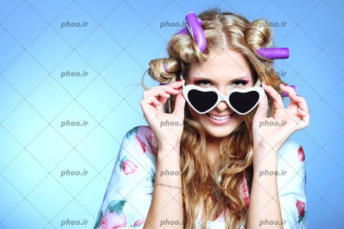 عکس زن عینکی درحال فر کردن موهای بلوندش در زمینه آبی