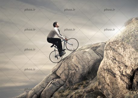 عکس با کیفیت مرد دوچرخه سوار در حال تلاش برای بالا رفتن از صخره