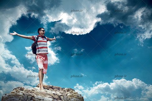 عکس با کیفیت مرد روی یک صخره بلند در برابر آسمان ابری