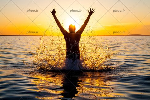 عکس با کیفیت شناگر در حال پریدن از آب دریا در طلوع گرم خورشید