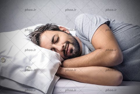 عکس با کیفیت مرد با لبخند خوابیده در رختخواب در پس زمینه خاکستری