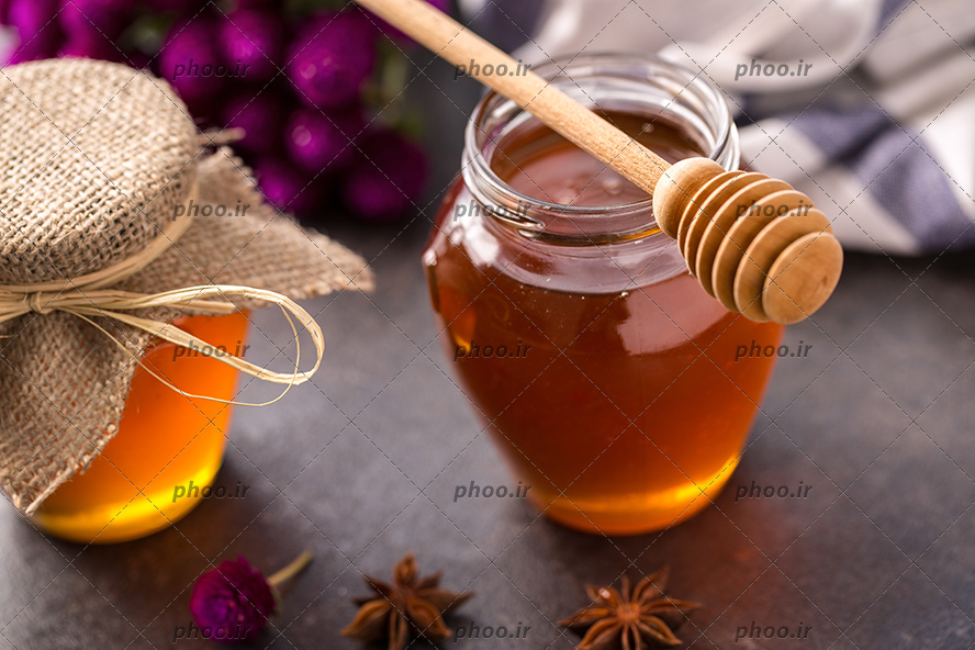 عکس ظرف شیشه ای از عسل و یک قاشق چوبی روی آن