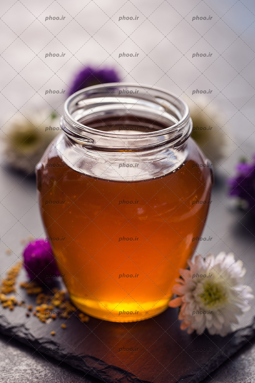 عکس ظرفی از عسل طبیعی در کنار گل های سفید و بنفش