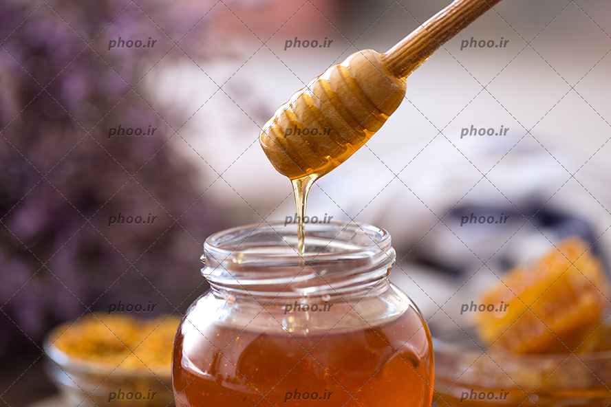 عکس برداشتن عسل از ظرف شیشه ای با قاشق چوبی