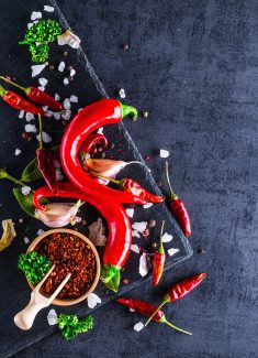 عکس فلفل های قرمز در کنار ادویه ترشی در کاسه چوبی در پس زمینه مشکی