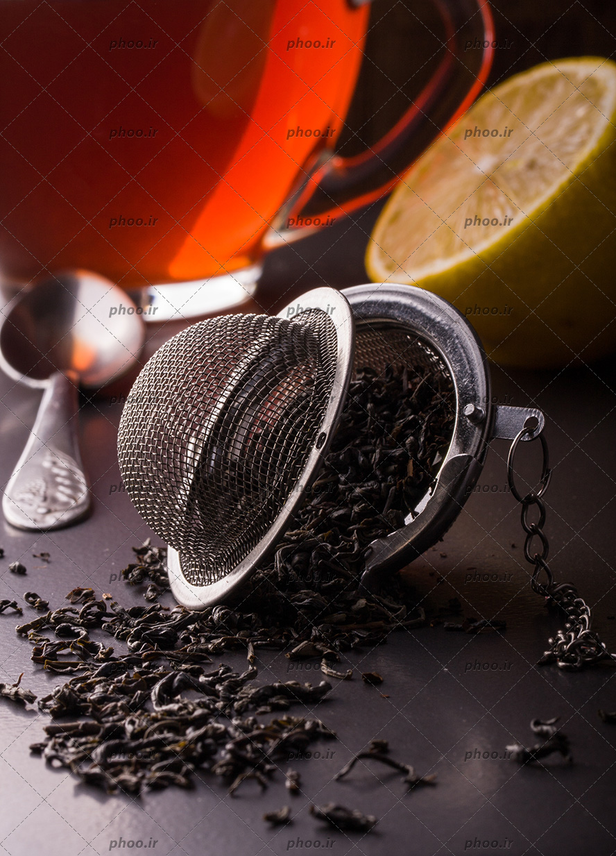 عکس صافی چای با چای خشک در کنار لیمو و فنجان چای در پس زمینه مشکی