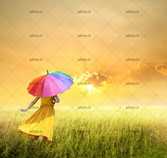 عکس خانم از پشت در حال دویدن در علفزار با چتر رنگی در دست در مقابل غروب خورشید