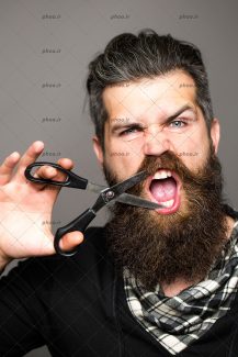 عکس مرد جوان با ریش و قیچی آرایشگری در دست بر روی صورت در پس زمینه خاکستری