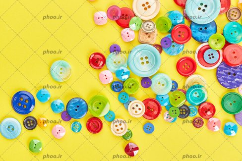 عکس دکمه های رنگی با ندازه ها و شکل های مختلف در پس زمینه زرد