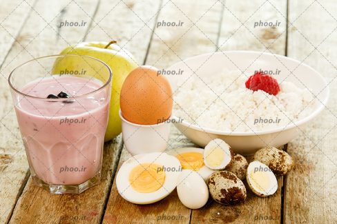 عکس تخم مرغ و تخم بلدرچین آب پز و شیر توت فرنگی و سیب در پس زمینه چوبی