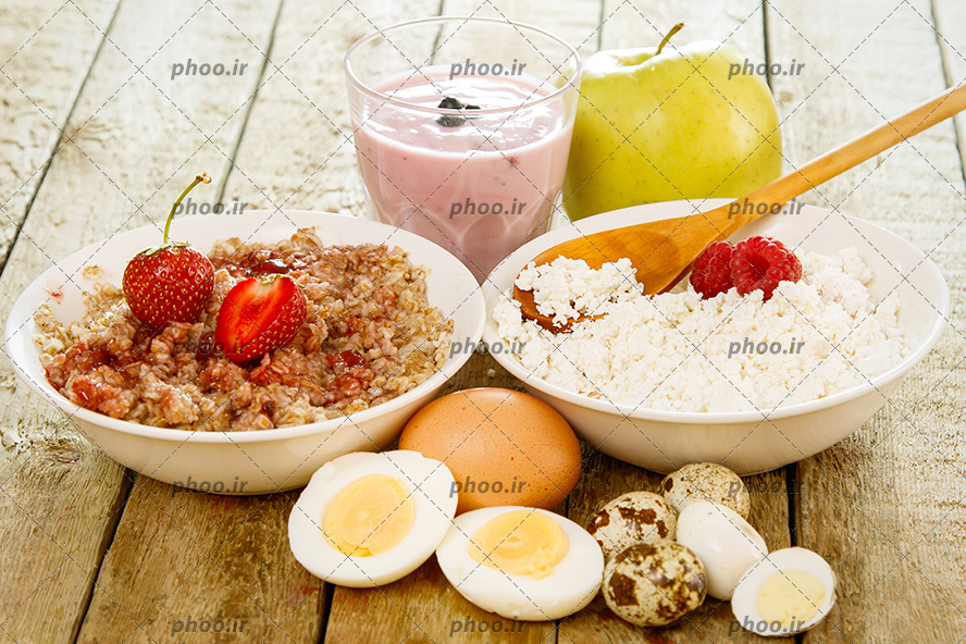 عکس تخم مرغ و تخم بلدرچین آب پز و شیر توت فرنگی و سیب و مربای توت فرنگی با جو دوسر در پس زمینه چوبی