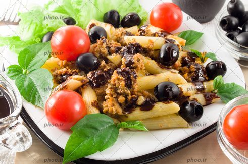 عکس پاستا پخته شده با تزئین زیتون و گوجه و سبزی در بشقاب سفید