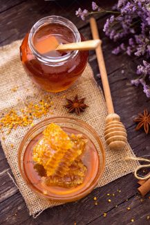 عکس عسل در ظرف و کاسه شیشه ای در کنار قاشق چوبی و گل بنفش