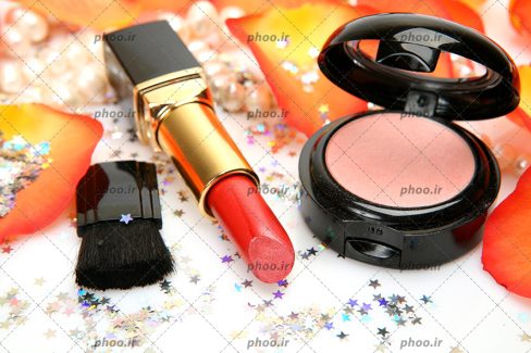عکس با کیفیت رژ قرمز در کنار رژگونه و براش کوچک در کنار اکلیل های ستاره ای و گلبرگ های نارنجی
