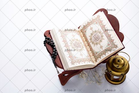 عکس با کیفیت قرآن بر روی لوح و تسبیح و فانوس و گل های زیبا در کنارش