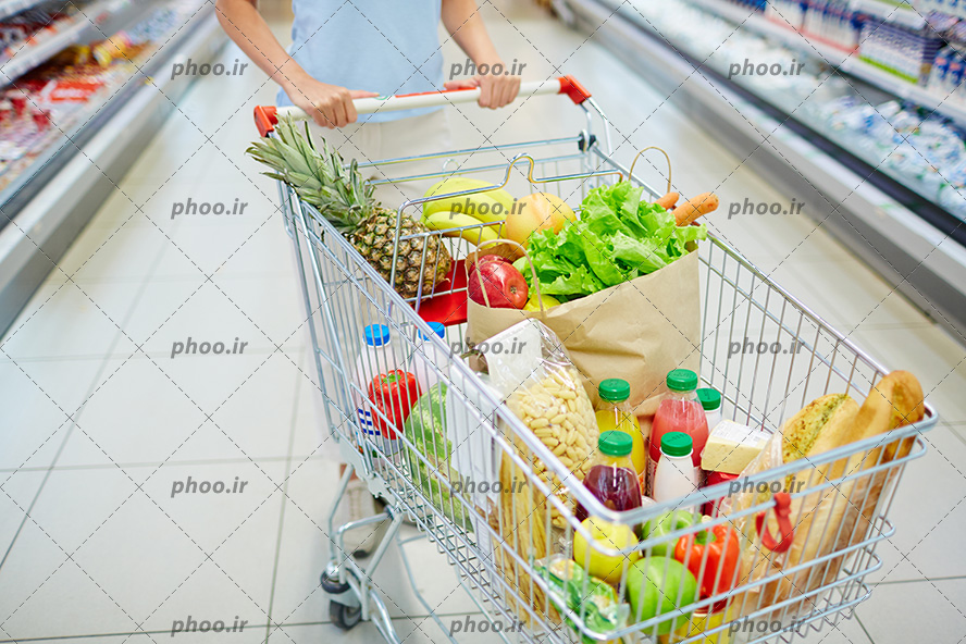 عکس با کیفیت مواد غذایی و سبزیجات و میوه ها داخل سبد خرید و سبد در دست زن ایستاده در فروشگاه