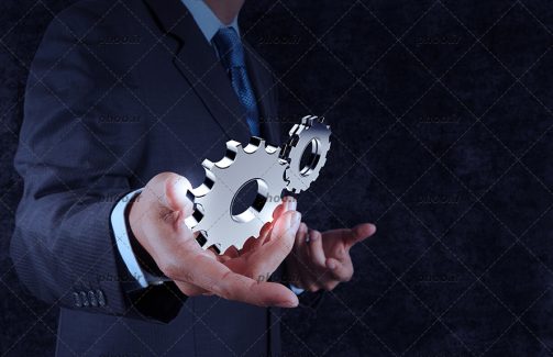 عکس با کیفیت چرخ دنده ها در دست مرد با کت در پس زمینه خاکستری
