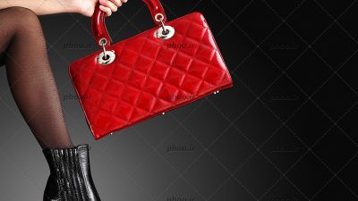 عکس با کیفیت خانم با کفش پاشنه بلند مشکی و کیف قرمز در دست در پس زمینه مشکی